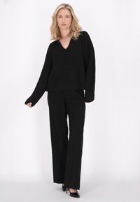 Maglione nero dalle linee morbide con scollo a V, abbinato a pantaloni neri a gamba larga e tacchi neri; texture liscia e design semplice.