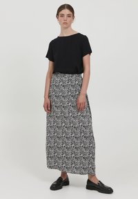 Černý top s krátkým rukávem spárovaný s dlouhou, vzorovanou sukní s černo-bílým abstraktním designem. Modelka má na sobě černé mokasíny.