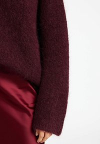 Burgundy, fluffig stickad tröja med lös passform och vida ärmar, kombinerad med en slät, mörkröd satinkjol. Mjuk textur och avslappnad design.