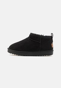 Botas de tobillo de ante negro con puntera redondeada, detalles de costura y una suela texturizada. Presenta una pequeña pestaña trasera y un parche de acento en contraste.