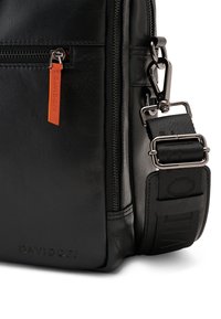 Schwarze Lederhandtasche mit strukturiertem Oberflächen, ausgestattet mit einem silbernen Reißverschluss und einem orangefarbenen Zugband. Verstellbarer schwarzer Stoffgurt mit Hardware-Details.