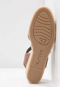 Sandale ouverte en suède marron avec un talon en jute naturel. La semelle en caoutchouc présente une texture striée et un marquage de taille 37.