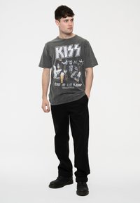 Black graphic t-shirt featuring a vintage KISS design, paired with black pants and black boots, standing on a plain white background.
