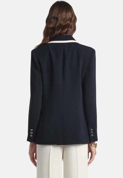 Tmavomodrý blejzer so štruktúrovanými ramenami, bielym lemom goliera a zlatými gombíkovými detailmi na rukávoch. Hladká tkanina s priliehavým strihom.