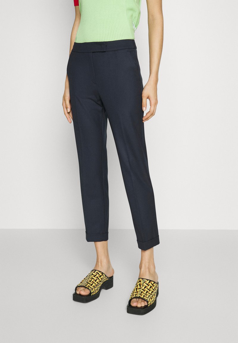 Navy skreddersydde bukser med oppbrett på ermet, kombinert med svarte og gule flettede slip-on sandaler med chunky hæl. Overdelen er grønn strikket.