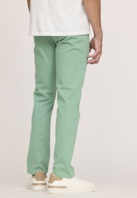 Pantalons vert menthe en tissu léger, design ajusté, avec une texture lisse et associés à des baskets blanches.