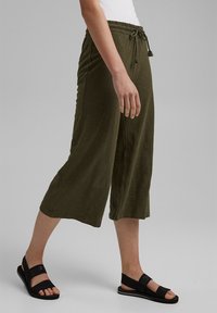 Culotte verde oliva in tessuto leggero con vita elastica e cordino. Abbinati a sandali neri con una fasciatura larga.