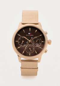 Brown watch with a round case, rose gold accents, textured beige strap, and multiple dials indicating day, date, and time.