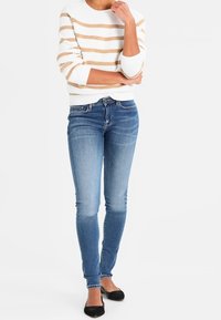 Suéter de punto a rayas blancas y beige con cuello redondo, combinado con vaqueros pitillo azul claro y zapatillas planas negras.