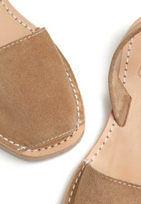 Sandalias de ante en color marrón claro con diseño de punta abierta, detalles de costura blanca y suela de cuero plana. Estilo simple y minimalista.