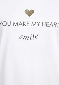 Weißes Baumwoll-T-Shirt mit einem goldenen Glitzerherz über dem Text "DU MACHST MEIN HERZ" und dem Wort "lächeln" in einer geschwungenen Schrift.