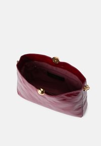 Bordeaux leren handtas met een glanzende afwerking. Heeft een ronde vorm en gouden hardware, waaronder een sluiting en een binnenvak.