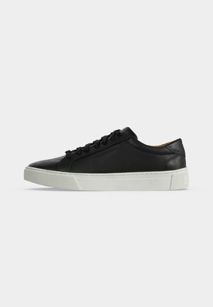 Schwarzer, niedriger Ledersneaker mit schwarzen Schnürsenkeln und einer dicken weißen Gummisohle, seitlich auf weißem Hintergrund gezeigt.