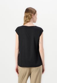 Top nero a maniche corte con scollo arrotondato, texture liscia e vestibilità comoda, abbinato a pantaloni beige a righe.