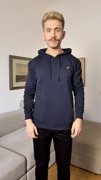 Sweatshirt azul-marinho com bolso canguru, tecido texturizado, cordões e um pequeno logótipo amarelo no peito. Usado com calças pretas.
