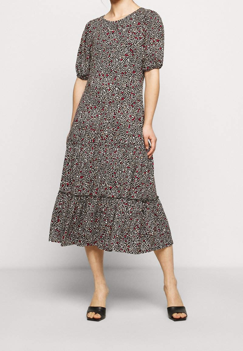 Vestido midi negro con un patrón floral en blanco y rojo. Confeccionado con mangas cortas abullonadas y un dobladillo con volantes. La tela parece ligera.