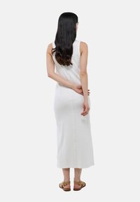 Robe midi blanche sans manches en maille côtelée avec une silhouette droite. Présente une couture au centre du dos et une texture subtile. Portée avec des sandales marron.