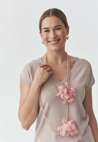 Colier floral roz cu flori din material și mărgele. Purtați peste un top bej deschis cu decolteu în V și mâneci scurte. Textură netedă.
