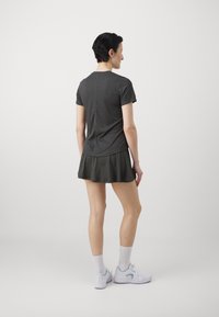 Vestido deportivo gris de mangas cortas con una falda de vuelo. Textura suave, parte superior ajustada y parte inferior fluida. Zapatillas deportivas blancas y calcetines hasta el tobillo.