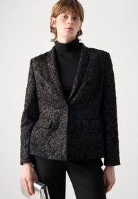 Zwarte textuur blazer met een bloemenpatroon, met notched revers en twee voorkruiden. Draag het over een zwarte coltrui.