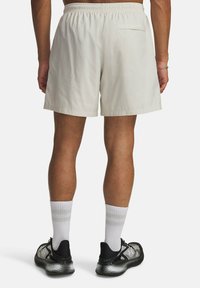 Pantalones cortos de color beige claro con cintura elástica, tejido texturizado y un bolsillo trasero. Llevados con calcetines blancos y zapatillas deportivas negras.