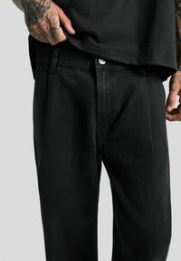 Schwarze Denim-Hose mit geradem Schnitt, ausgestattet mit einem Knopfverschluss, einer Druckdetailverarbeitung und einer weichen, strukturierten Oberfläche.