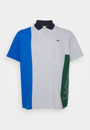 Polo avec des blocs de couleurs gris, bleu et vert, manches courtes, col bleu marine et logo brodé en vert sur le côté.