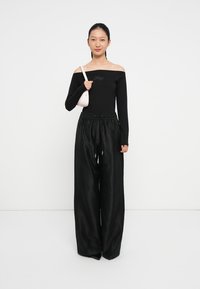 Čierny off-shoulder top s dlhými rukávmi, kombinovaný s voľnými čiernymi nohavicami s elastickým pásom. Modelka drží malú ružovú kabelku.