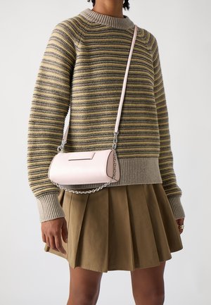 Henkilö, jolla on yllään raidallinen neulepaita, laskostettu ruskea hame ja vaaleanpunainen olkalaukku, jossa on ketjuyksityiskohta, kannettuna halki vartalon.