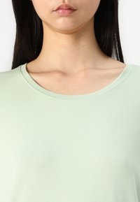 Hellgrünes Kurzarm-T-Shirt mit rundem Halsausschnitt und glatter Textur, das ein einfaches, minimalistisches Design zeigt.
