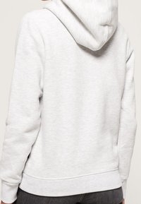 Felpa grigia heather con una texture morbida, dotata di cappuccio arrotondato e orlo a costine, progettata per un abbigliamento casual.