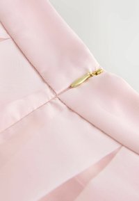 Tela de satén rosa claro con una textura suave y una cremallera oculta con una lengüeta de tirador dorada, situada a lo largo de la costura.