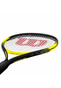 Raqueta de tenis amarilla y negra con un marco ancho, que presenta una superficie de cuerdas blanca y un logo rojo en el centro, mango de agarre texturizado en negro.