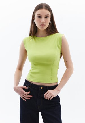 Groene geribbelde mouwloze top met een ronde halslijn, getailleerde pasvorm en inzetdetails, gecombineerd met donkere spijkerbroeken.