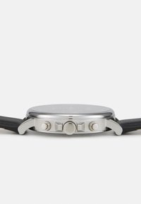 Montre chronographe avec un boîtier en acier inoxydable, un bracelet en cuir noir, des accents argentés et un verre transparent, dotée de trois poussoirs sur le côté.