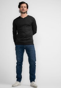 Zwarte lange mouw V-hals trui gecombineerd met blauwe jeans en witte sneakers. De trui heeft een getailleerd ontwerp en geribbelde manchetten.
