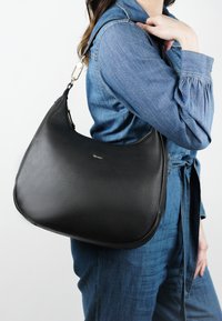 Zwarte leren schoudertas met een gladde textuur, gebogen vorm en gouden hardware. Gekocht over een denim outfit.