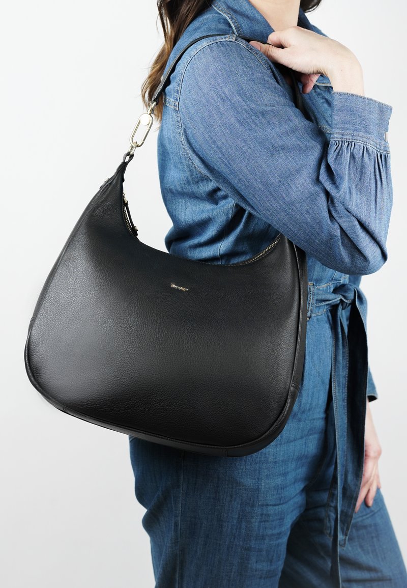 Zwarte leren schoudertas met een gladde textuur, gebogen vorm en gouden hardware. Gekocht over een denim outfit.