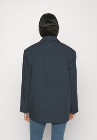 Ciemnoniebieski, oversize'owy blezer z wyłogowym kołnierzem, zapinany na guziki mankietami i lekko zaokrąglonym dołem. Gładki materiał z minimalnymi detalami marki.