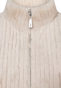 Beiger Kunstpelz mit Struktur, hoher Kragen und durchgehendem Reißverschluss vorne mit silbernem Zuglaschen und vertikal geripptem Design.