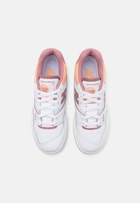 Baskets blanches avec des accents roses et oranges, présentant une tige en cuir lisse, un col rembourré et un logo contrastant sur le côté.