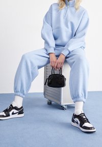 Helles blaues Sweatshirt mit einem halben Reißverschluss und passender Jogginghose, kombiniert mit schwarz-weißen Turnschuhen und einer kleinen schwarzen Handtasche.
