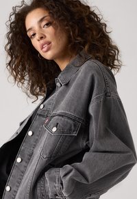 Gray denim jacket with oversized fit, featuring silver buttons, two front pockets, and visible stitching. Soft texture and relaxed design.