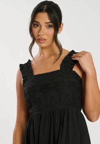 Svart klänning med fyrkantig halsringning och volangärmar. Tyget har broderade palmer och en utsvängd kjol.