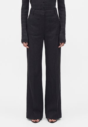 Pantaloni neri a vita alta e gamba larga con tasche applicate sul davanti, indossati con un top a maniche lunghe a coste scuro e sandali neri con punta aperta.