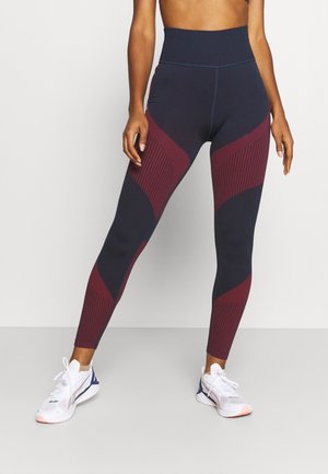 Leggings taille haute en marine avec des panneaux géométriques bordeaux. Texture lisse et design ajusté, avec des accents rayés sur les côtés.