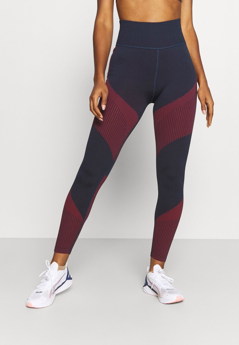 Leggings de tiro alto en azul marino con paneles geométricos en burdeos. Textura suave y diseño ceñido, con acentos a rayas a lo largo de los laterales.