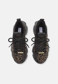 Baskets noires et dorées ornées de clous avec des lacets noirs, des semelles épaisses et une étiquette "NY90" sur la languette, vues de dessus sur un fond blanc.