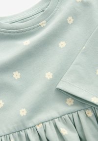 Robe en coton bleu clair avec petits motifs floraux crème, encolure ronde, manches courtes et jupe froncée. Texture lisse.