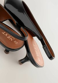 Schwarze Lackleder-Slingback-Pumps mit moderatem Absatz, die eine glatte Oberfläche, gepolsterte Innensohle und eine Markenkennzeichnung auf der Fußbett haben.